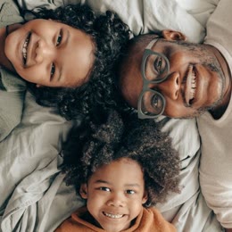 A father and his two children lying on a bed, smiling up